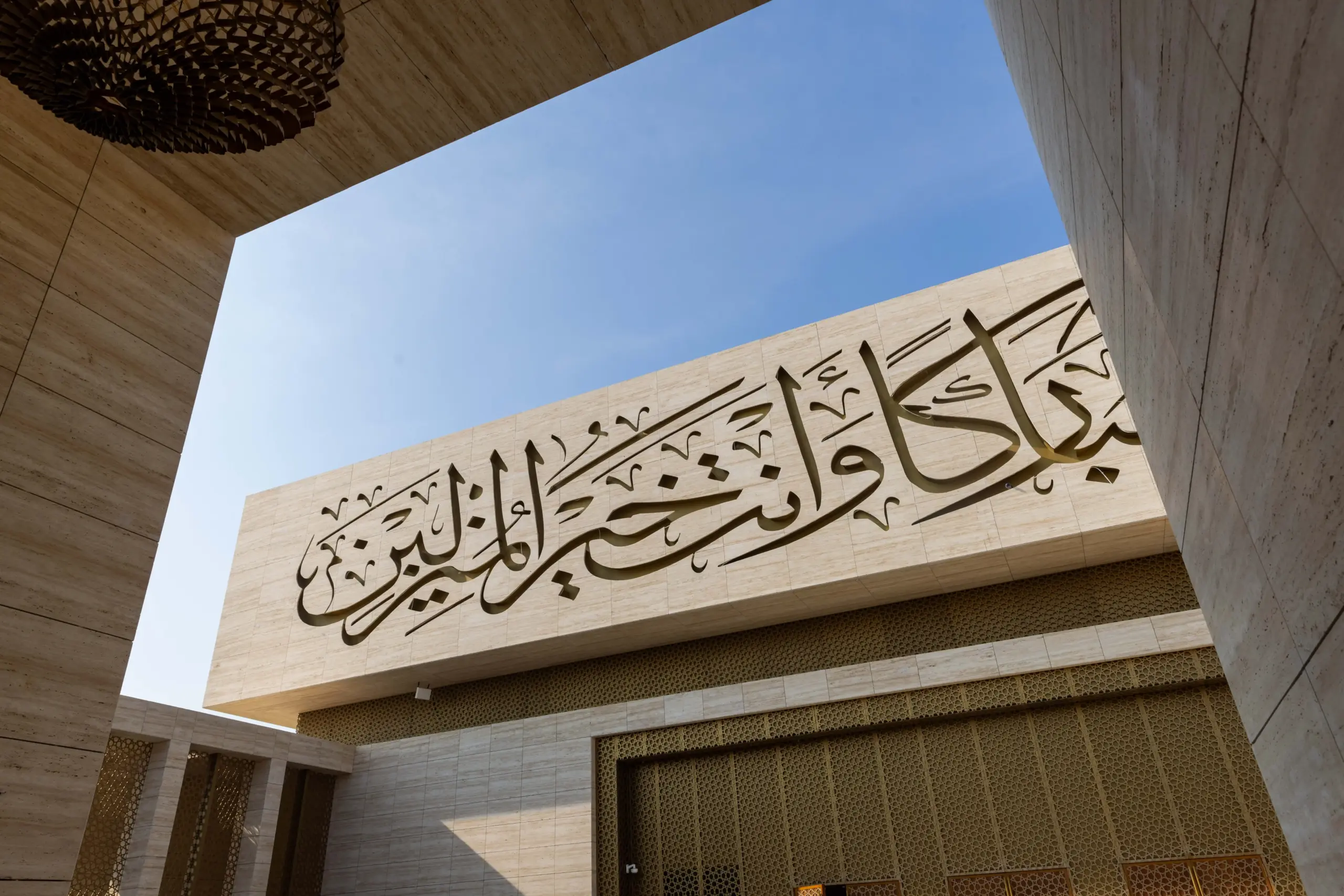 A close-up of mosque twenty seven architectural surface perforated with bright, illuminated Arabic calligraphy, suggesting a modern Islamic design feature.