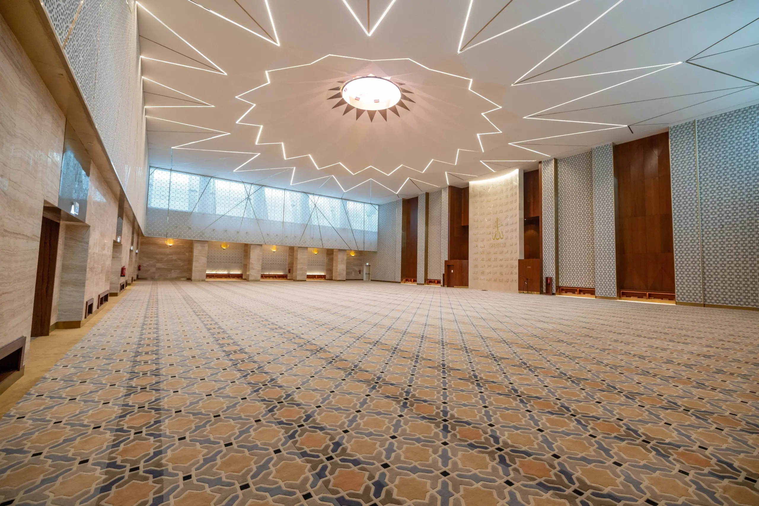 Interior hallway at Mosque Twenty-Seven with dark wood paneling, white walls, and a detailed white-and-gray Islamic geometric patterned floor