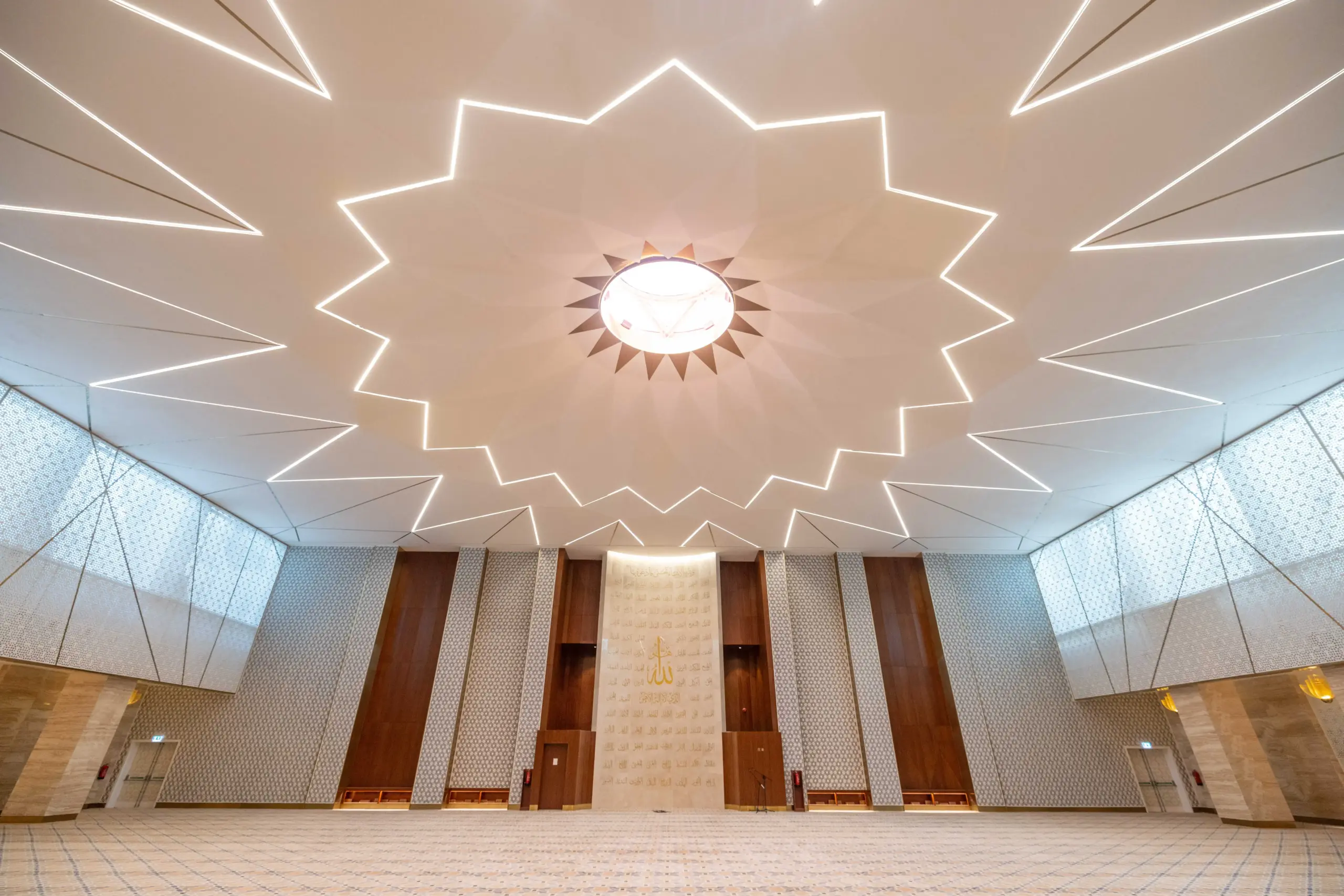Interior hallway at Mosque Twenty-Seven with dark wood paneling, white walls, and a detailed white-and-gray Islamic geometric patterned floor